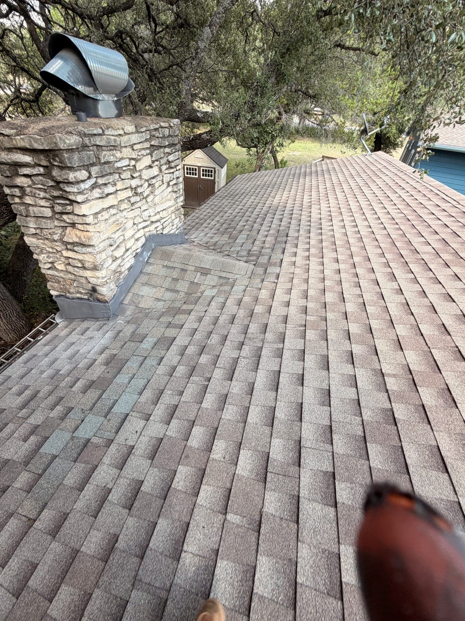 Completed stone chimney with counter flashing let into the masonry and fresh shingle courses run tight to the base