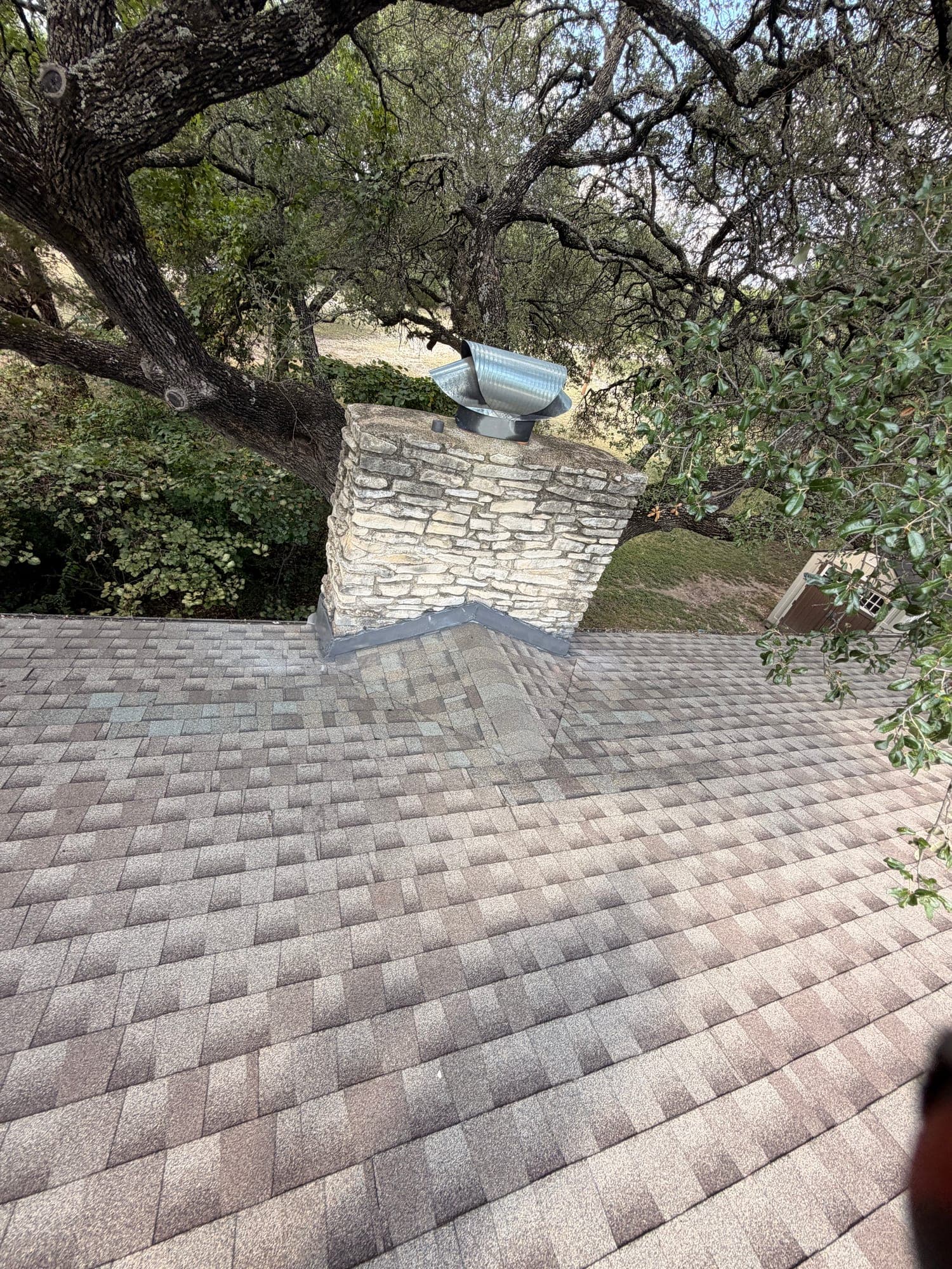 Finished cricket built behind a stone chimney to divert water around it, shingles run into new counter flashing on both sides