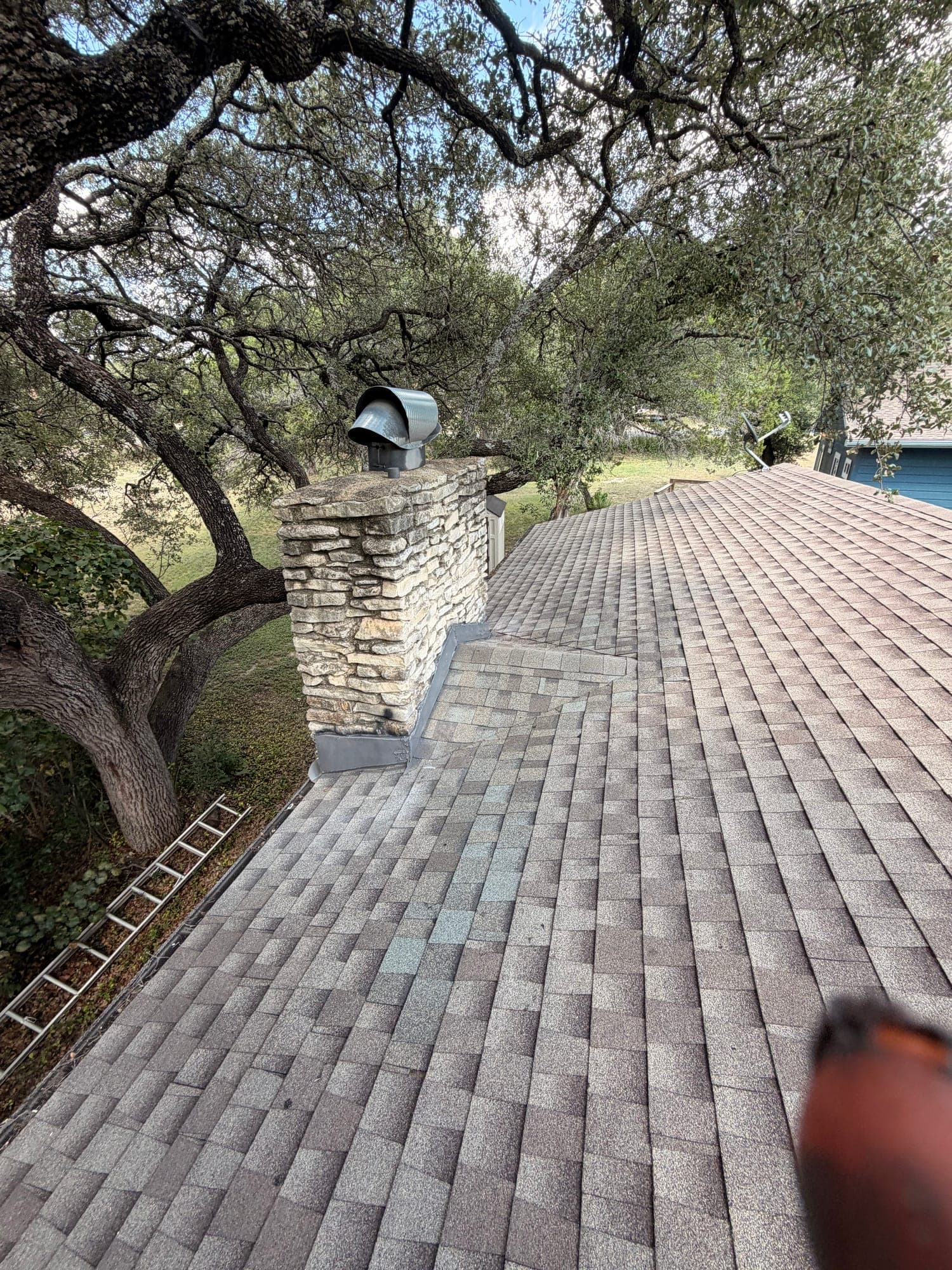 Long finished shingle run passing the rebuilt stone chimney, ladder still standing at the eave