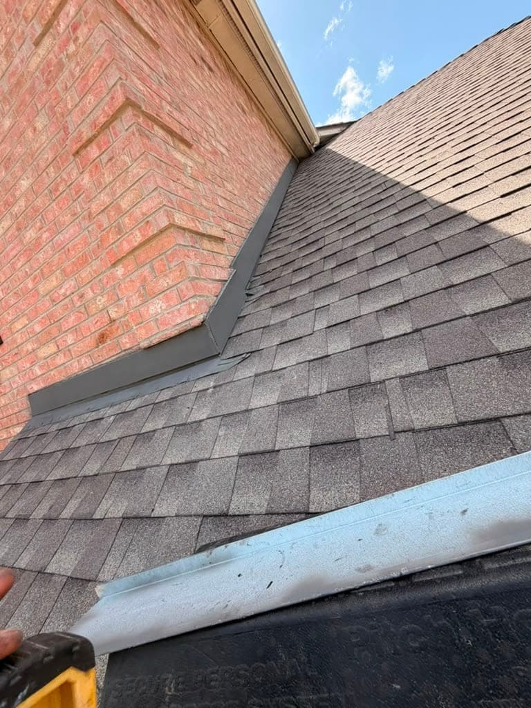 New continuous flashing and counter flashing installed along a brick sidewall with fresh shingle courses run into it