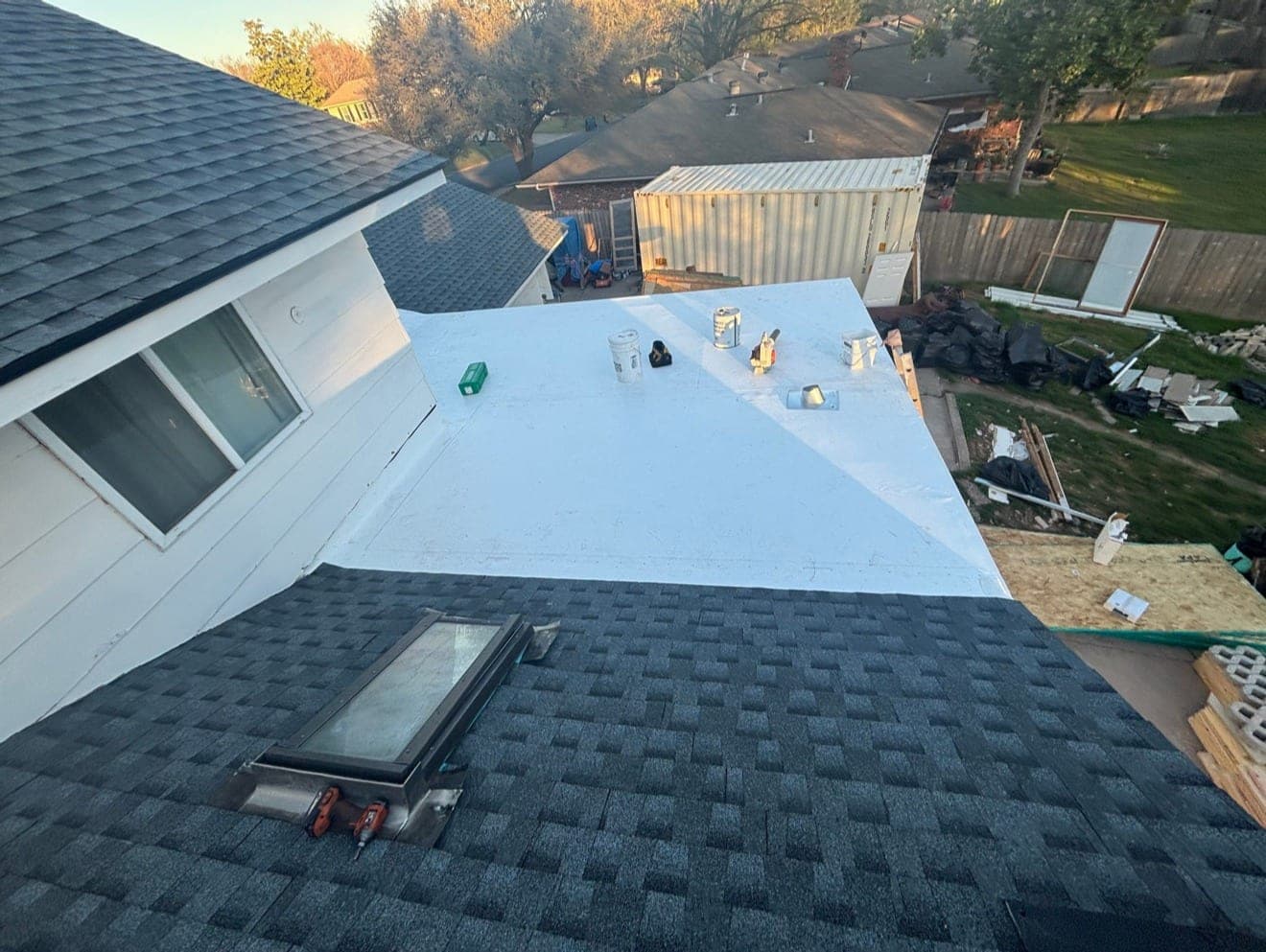 White membrane roof over a low-slope section meeting a steep architectural shingle field, skylight in the foreground