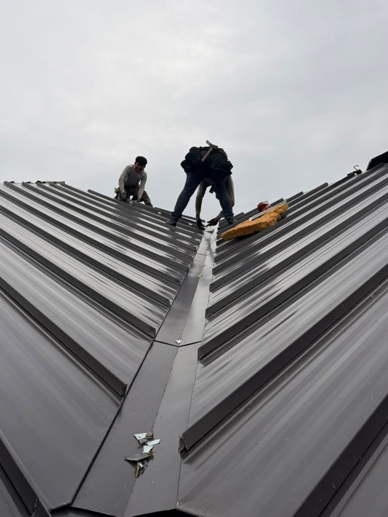 Two crew members working the ridge of a dark standing seam metal roof