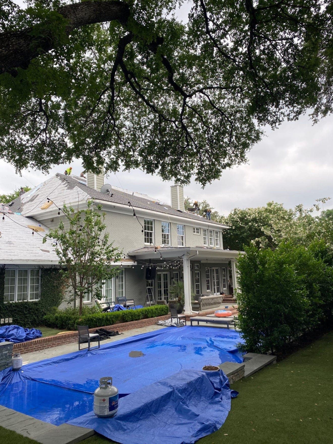 Blue tarps covering an entire pool, the patio furniture and the hedges while the crew tear off the roof of the house behind