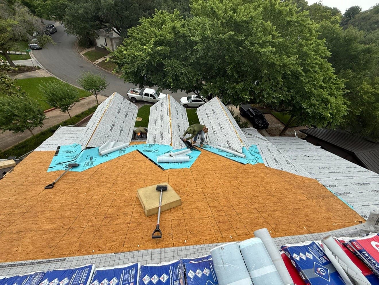 Elevated view of a fully redecked roof with synthetic underlayment being run up the dormers and shingle bundles staged along the ridge