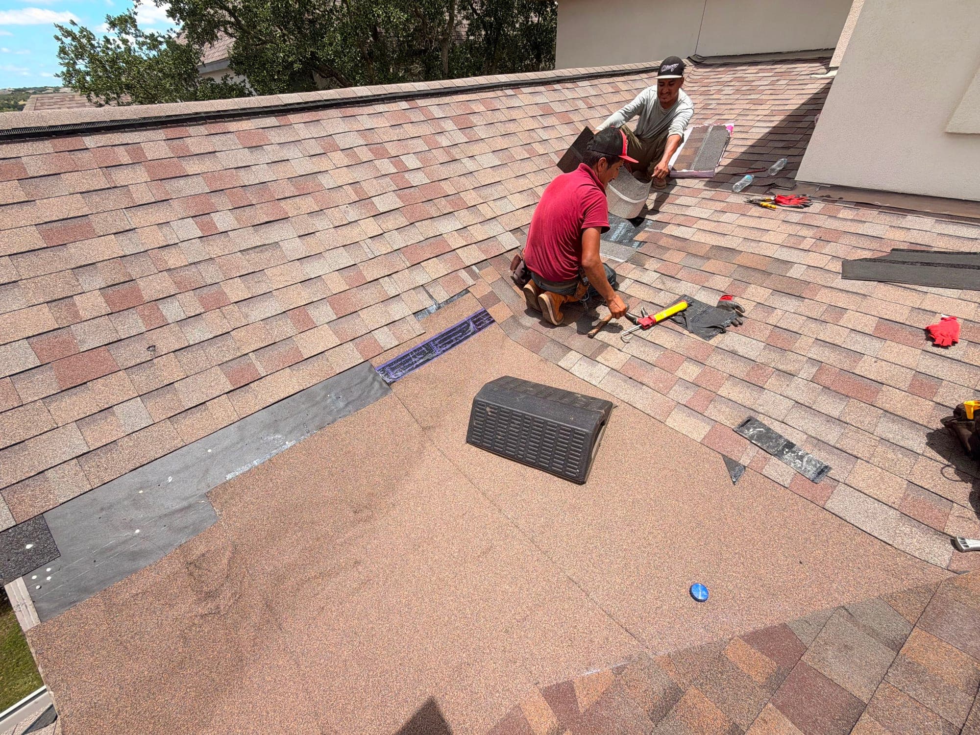 Two roofers working a shingle field, cutting and setting cap along the ridge