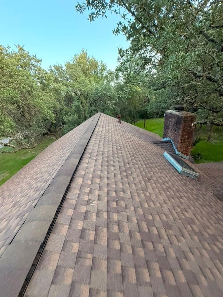 Long finished shingle ridge running toward a brick chimney with new counterflashing