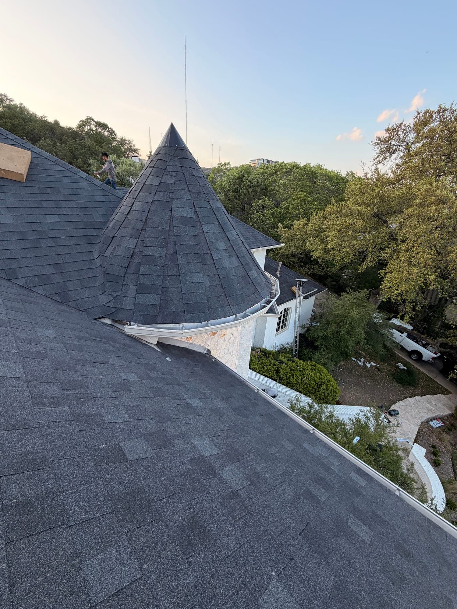 Conical turret roof fully shingled at golden hour, crew member walking the ridge behind it
